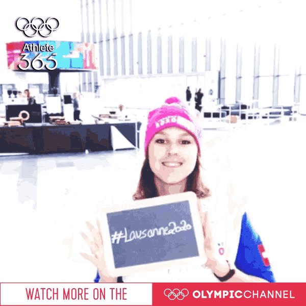 a woman in a pink hat holds up a sign that says # lausanne2020
