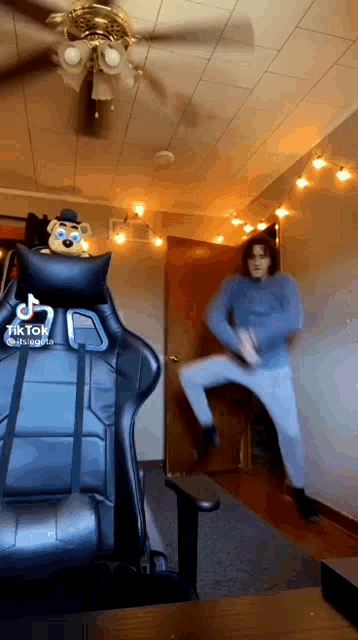 a man is dancing in a room with a ceiling fan and a teddy bear on a chair .