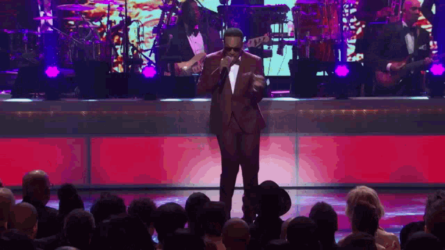 a man in a tuxedo is singing into a microphone on stage