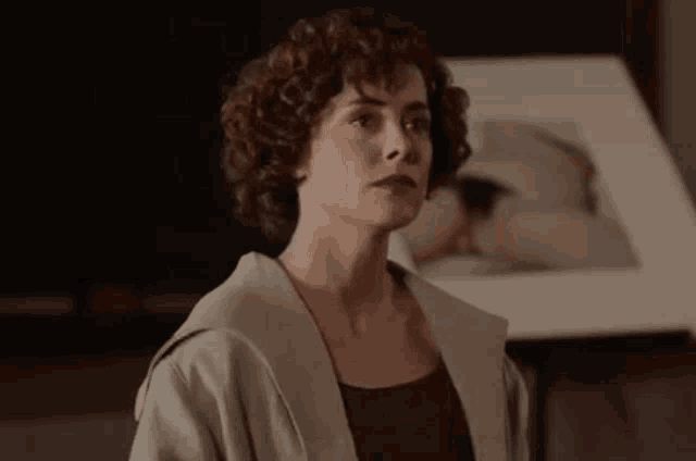 a woman with curly hair is standing in front of a framed picture of a woman .