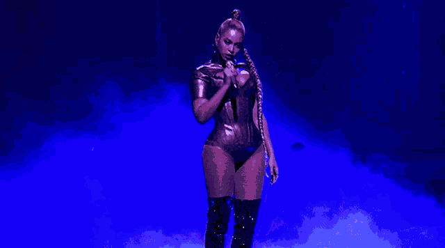 a woman in a bodysuit and over the knee boots is standing on a stage .