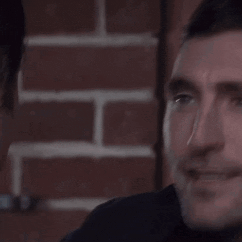 a close up of a man 's face with a brick wall in the background