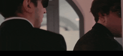 two men in suits are standing next to each other in front of a mirror .