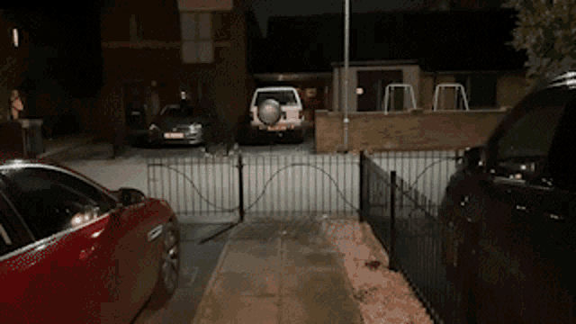a red car is parked in front of a fence