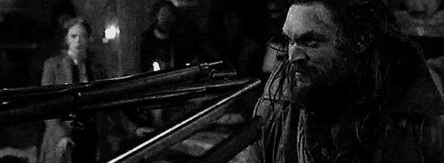 a black and white photo of a man holding a gun in a dark room .