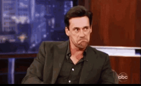 a man in a suit and black shirt is making a funny face while talking on a television show .