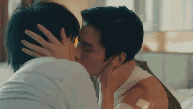 two men are kissing each other on the forehead in a bedroom .