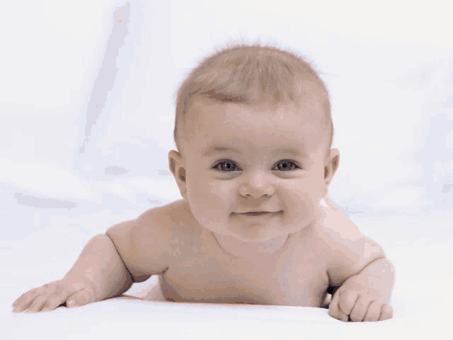 a baby is smiling while laying on its stomach on a white surface