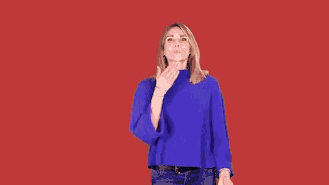 a woman in a blue sweater is blowing a kiss against a red background .