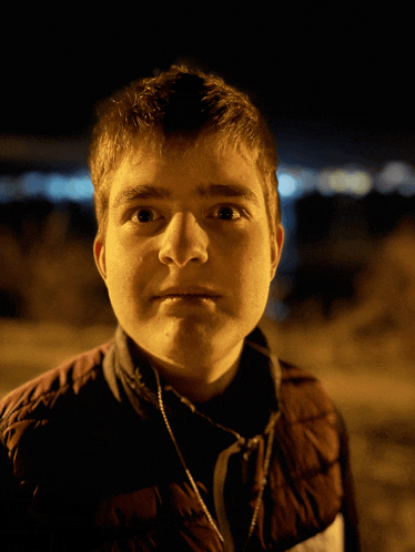 a young man wearing headphones looks at the camera at night