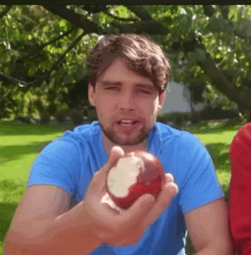 a man in a blue shirt is holding an apple in his hand