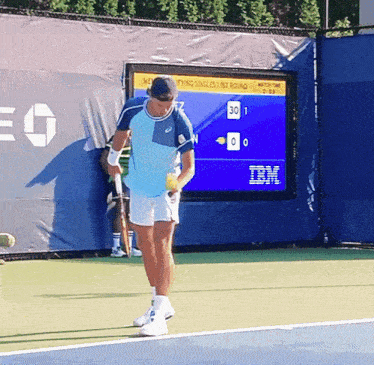 a man stands on a tennis court in front of a scoreboard that says ibm on it
