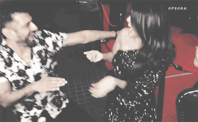 a man and a woman are dancing on a red carpet with opsora written on the bottom of the image