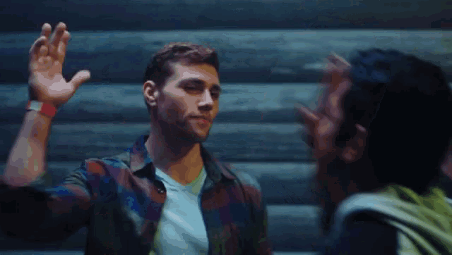 a man in a plaid shirt is waving his hand at another man