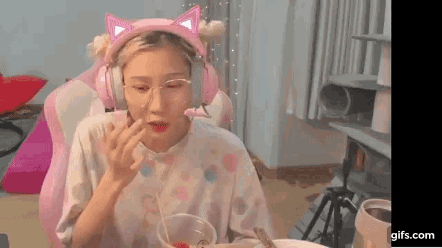 a woman wearing headphones and glasses is eating a strawberry from a cup .
