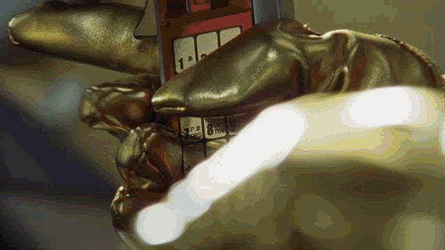 a gold glove is holding a red cell phone with the numbers 1 through 9 on it
