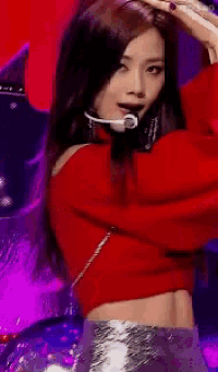 a woman wearing a red sweater and a microphone is dancing on a stage