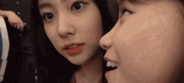 two girls are looking at each other in the mirror and one has red lipstick on her lips