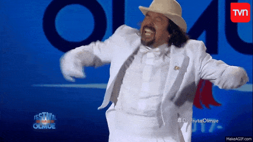 a man in a white suit and hat is dancing in front of a sign that says festival olmue