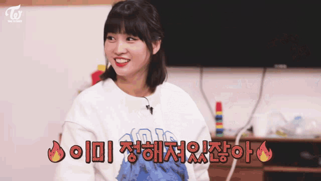 a woman wearing a twice sweatshirt is smiling in front of a flat screen tv