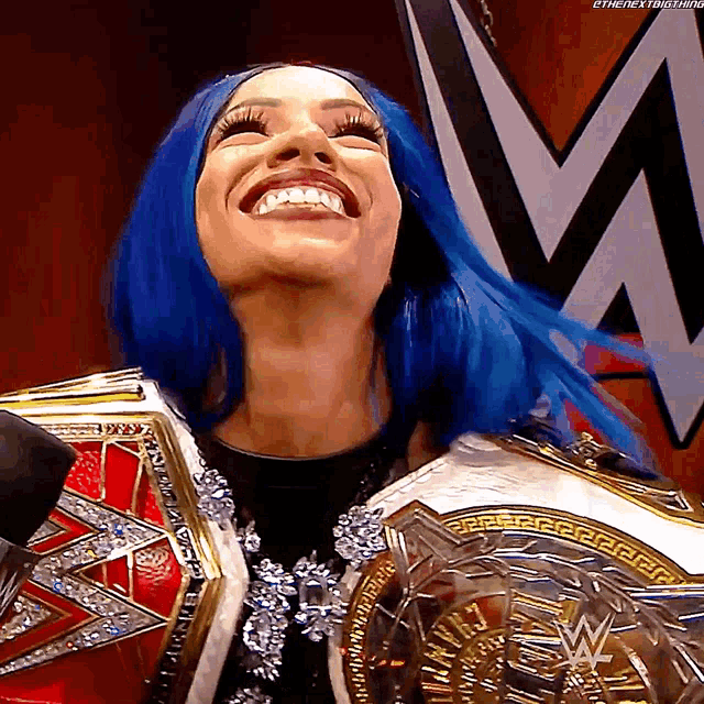 a woman with blue hair is smiling and holding a wrestling championship belt