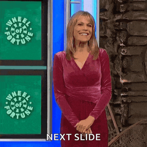 a woman in a red dress is smiling while standing in front of a wheel of fortune logo .
