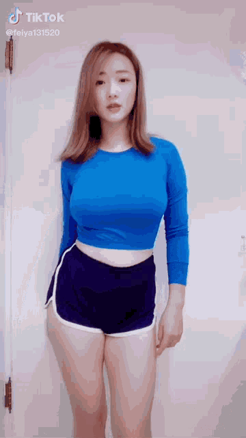 a woman in a blue crop top and shorts is standing in front of a white wall .