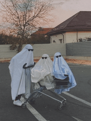 three people dressed as ghosts push a shopping cart
