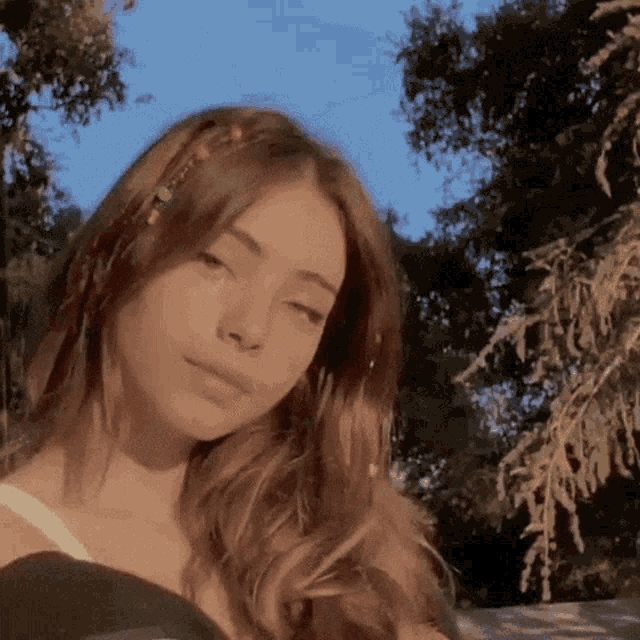 a girl with long brown hair is standing in front of a tree .