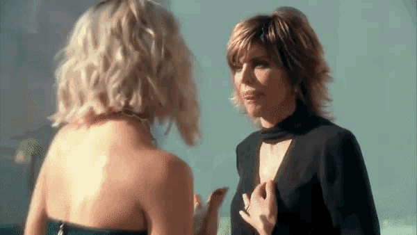 two women are standing next to each other and talking to each other . one of the women is wearing a black dress .