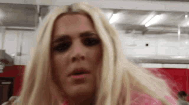 a woman with blonde hair is wearing a pink shirt and making a funny face