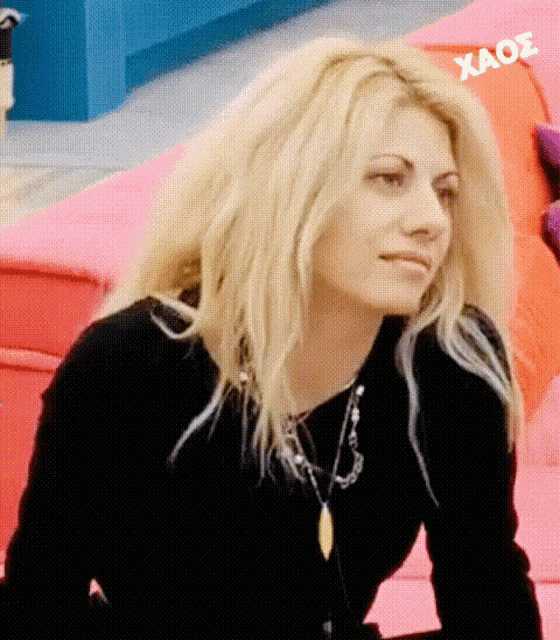 a woman with blonde hair is wearing a black shirt and a necklace with the word xaos on the bottom