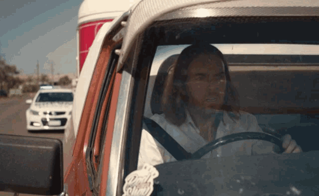 a man with long hair is driving a car with a sticker on the windshield that says ' jesus ' on it