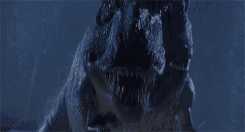 a close up of a dinosaur with its mouth open in the rain in the dark .