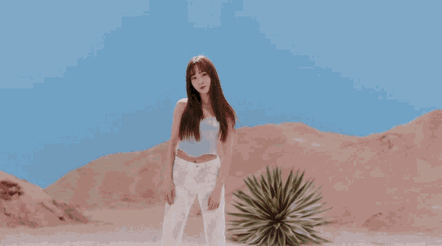 a woman in a purple top and white pants is standing next to a cactus in the desert