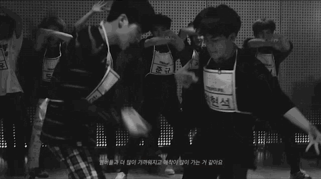 a black and white photo of a group of young men dancing in a room .