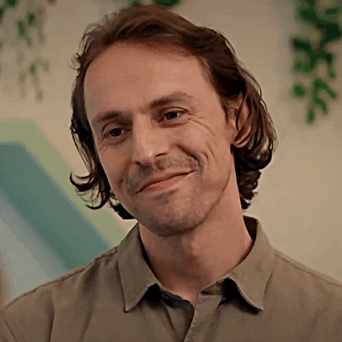 a man with long hair is smiling and wearing a tan shirt