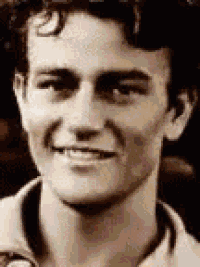 a young man with curly hair is smiling for the camera in a black and white photo .