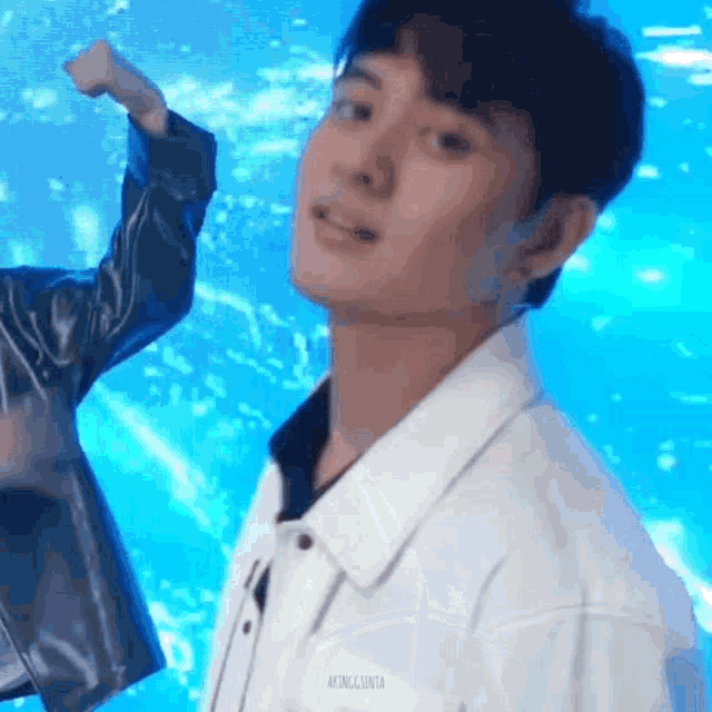 a young man in a white jacket is standing in front of a blue background and looking at the camera .