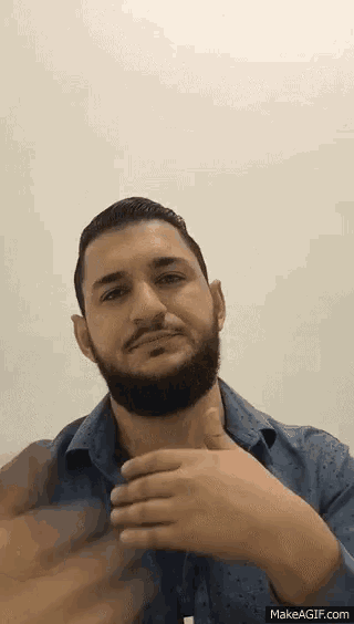 a man with a beard and a blue shirt is giving a thumbs up .