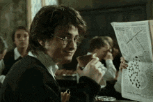 harry potter is reading a newspaper and drinking from a cup