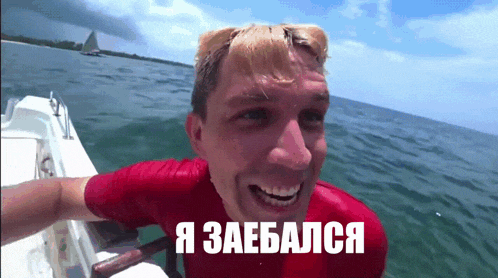 a man in a red shirt is sitting on a boat in the ocean with a caption in russian