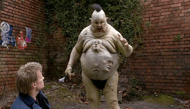 a man stands in front of a brick wall looking at a statue of a monster