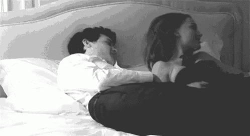 a black and white photo of a man and a woman laying in bed .