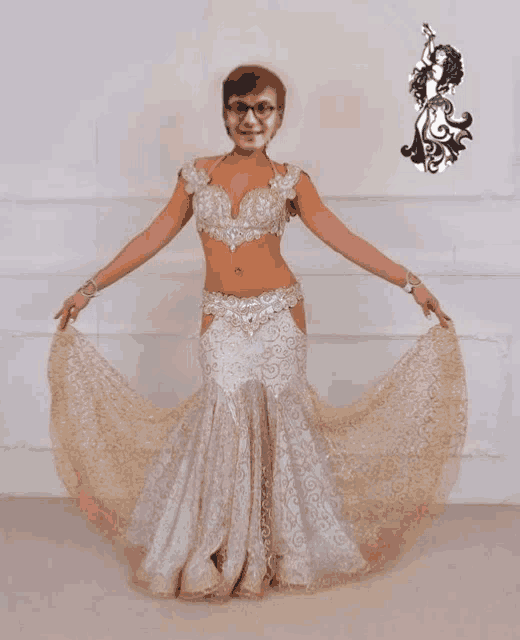 a woman in a white and gold dress with a picture of a belly dancer on the wall