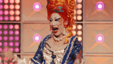 a drag queen is wearing a blue and white dress and a red wig and pearls .