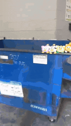 stuffed animals are sitting on top of a blue dumpster that says ' recycle ' on it