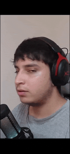 a man wearing headphones and a grey shirt is looking at a microphone