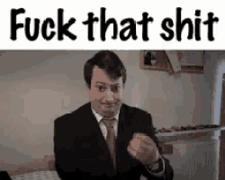 a man in a suit and tie is sitting at a table with his fist in the air and the words `` fuck that shit '' .