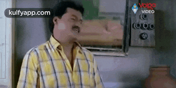 a man in a plaid shirt is making a funny face while standing in a room .